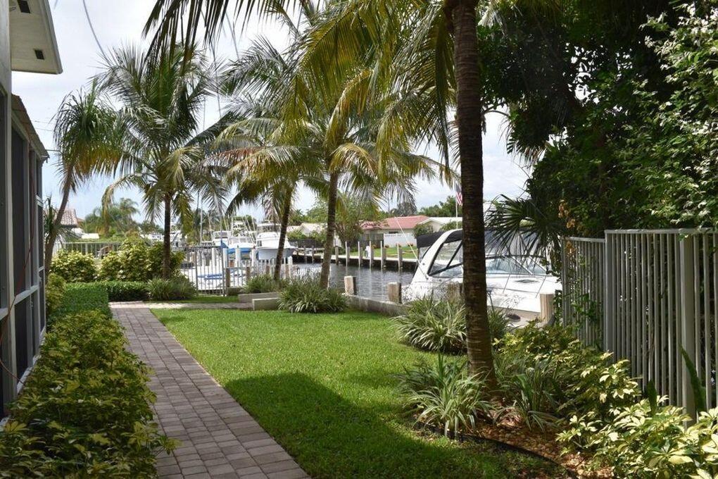 A grassy backyard with a brick walkway leads toward a canal with docked boats — 1361 NE 27 Way, Pompano Beach FL 33062, POMPANO BEACH, FL