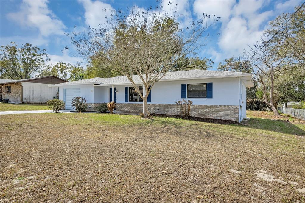 A single-story house with white siding, a brick base, and blue shutters under a cloudy sky — 606 THIRD AVENUE, LADY LAKE, FL