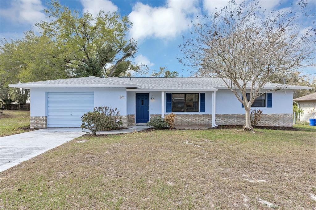 A light blue single-story house features a brick base, a garage, and dark blue shutters — 606 THIRD AVENUE, LADY LAKE, FL