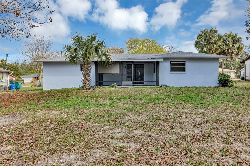 The rear exterior of a single-story house features a screened-in porch and a palm tree — 606 THIRD AVENUE, LADY LAKE, FL