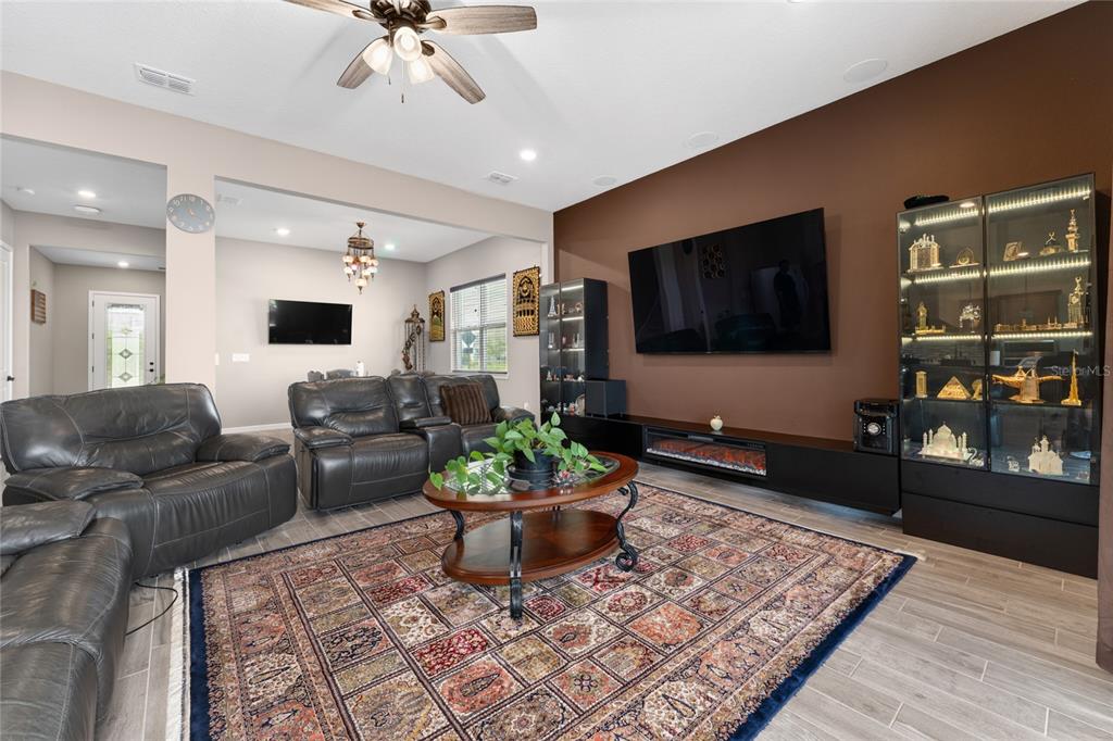 A living room features a large television, a fireplace console, display cabinets, and a patterned rug — 13615 RITTA ISLAND DRIVE, ORLANDO, FL