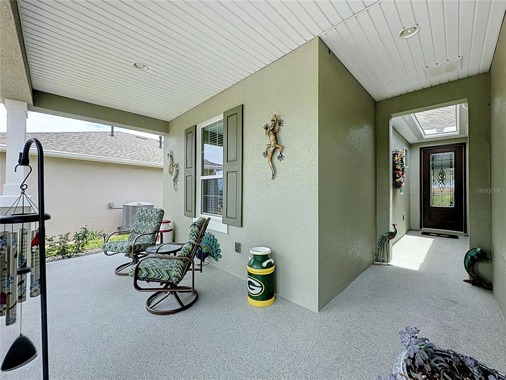 A covered porch features two chairs, a Green Bay Packers milk can, and gecko wall decor — 552 NARROW VIEW LANE, GROVELAND, FL