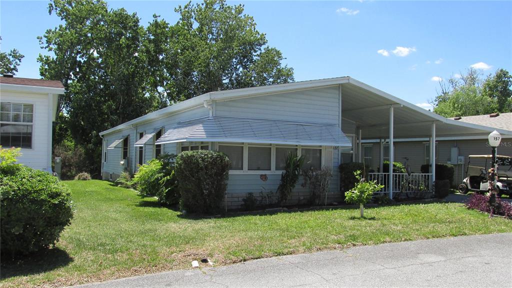 A light blue manufactured home with a metal carport and white window awnings — 157 VICTORIA DRIVE, HAINES CITY, FL