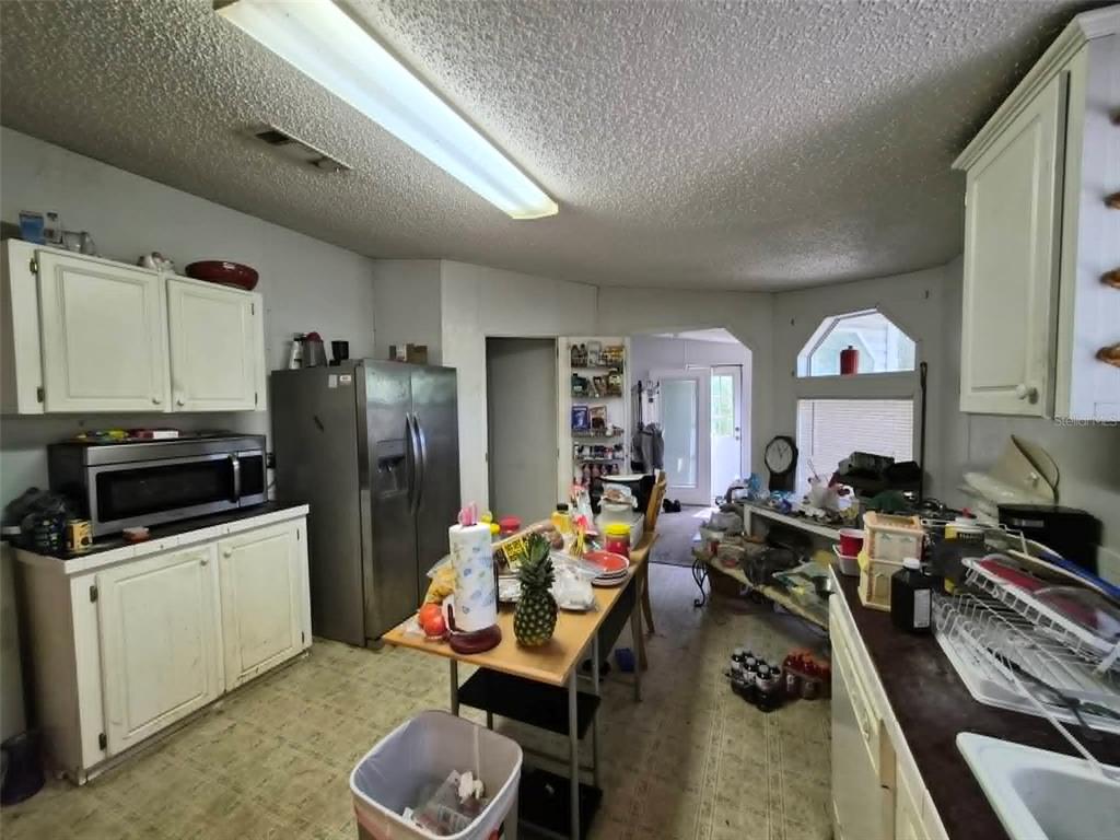 A cluttered kitchen features white cabinets, a stainless steel refrigerator, and a central island — 21508 NW 190TH AVENUE, HIGH SPRINGS, FL
