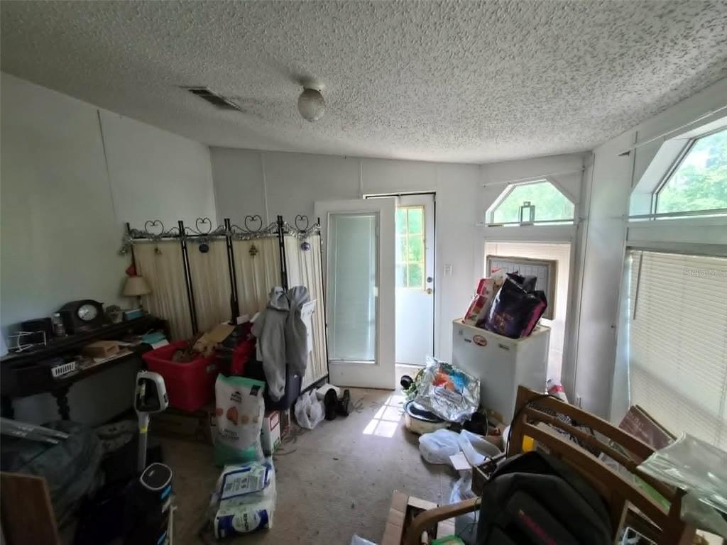 A cluttered room with a popcorn ceiling, white walls, and a door leading outside — 21508 NW 190TH AVENUE, HIGH SPRINGS, FL