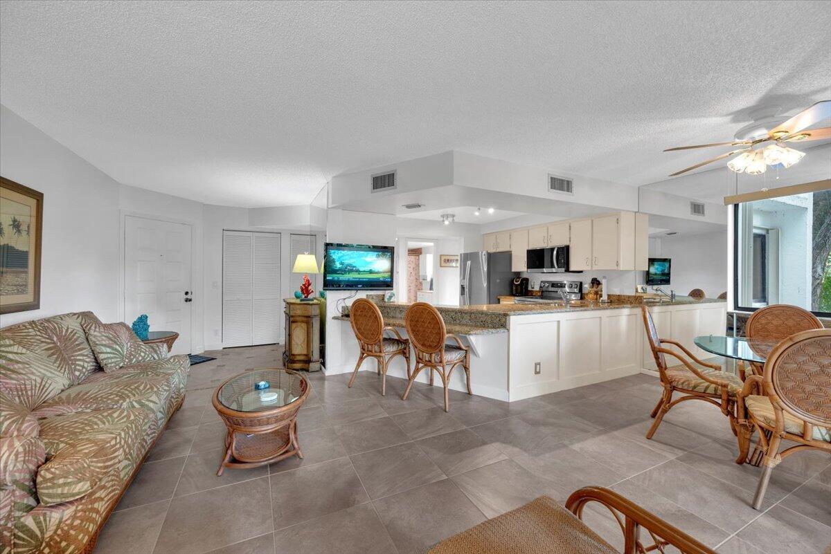 An open-concept living and dining area with tile floors, rattan furniture, and a granite kitchen — 1605 S Us Highway 1 # E201, Jupiter FL 33477, JUPITER, FL