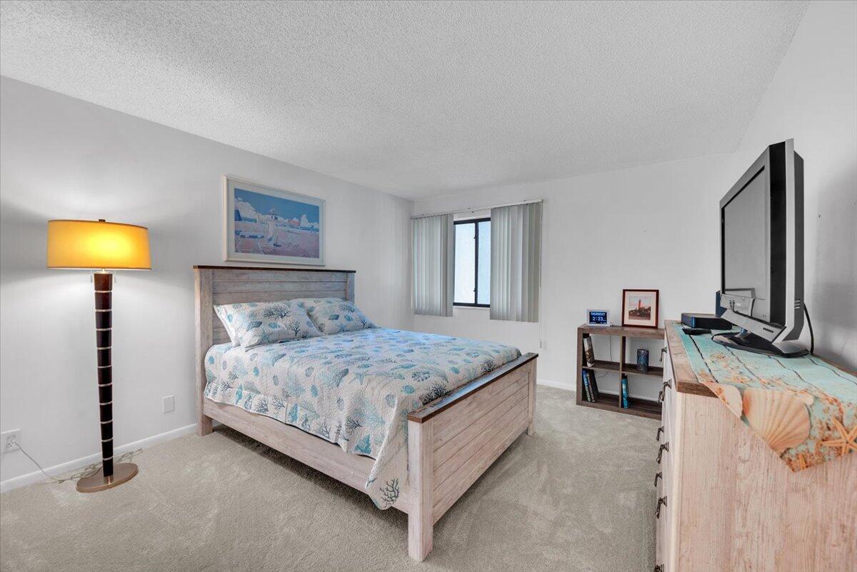 A bedroom features a wooden bed frame, a floor lamp, and a dresser with a television — 1605 S Us Highway 1 # E201, Jupiter FL 33477, JUPITER, FL