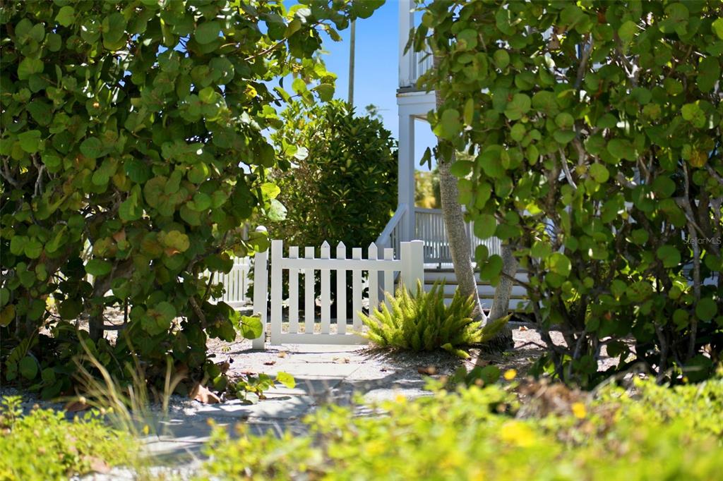 A white picket gate stands at the end of a path surrounded by lush greenery — 106 2ND AVENUE, ST PETE BEACH, FL