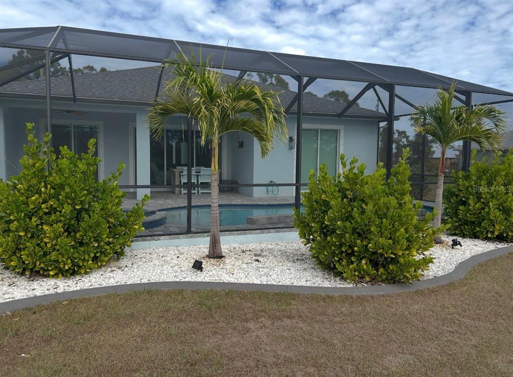 A backyard pool area is enclosed by a screen cage with palm trees and landscaping — 109 FLOWER ROAD, ROTONDA WEST, FL