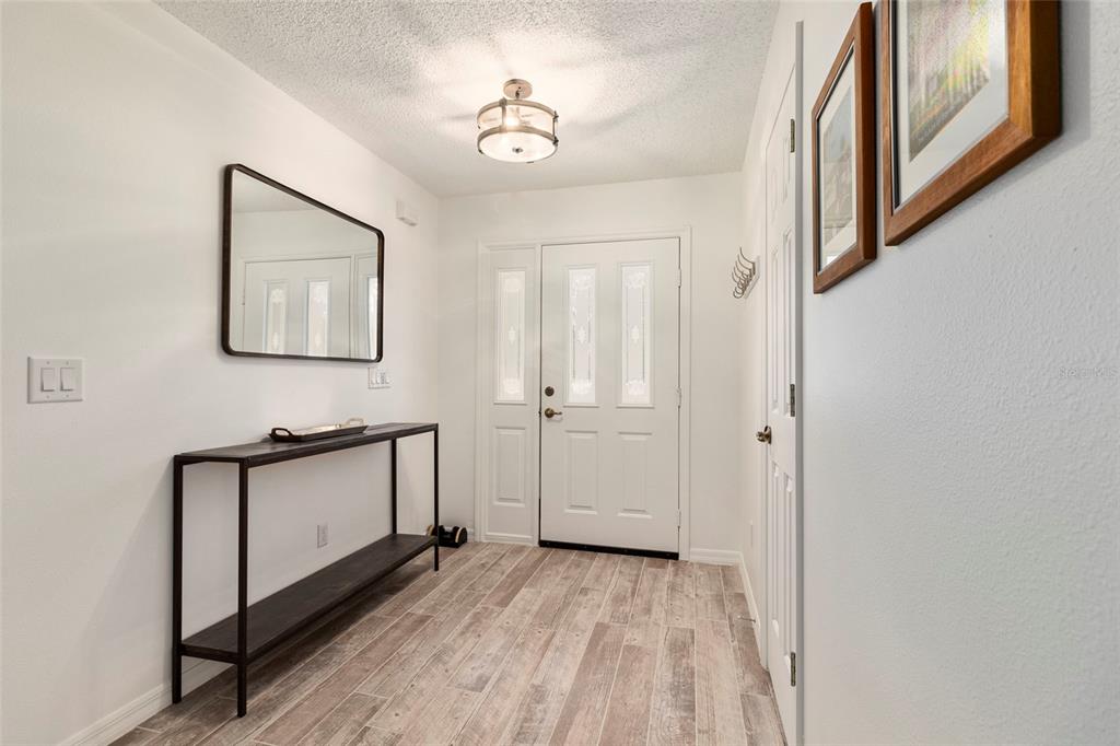 A bright entryway features a console table, a wall mirror, and light wood-look tile flooring — 1900 NW 73RD TERRACE, OCALA, FL