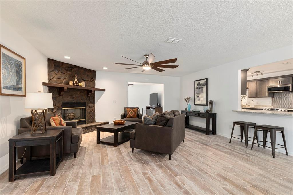 A living room with a stone fireplace, wood-look tile flooring, and an open kitchen pass-through — 1900 NW 73RD TERRACE, OCALA, FL