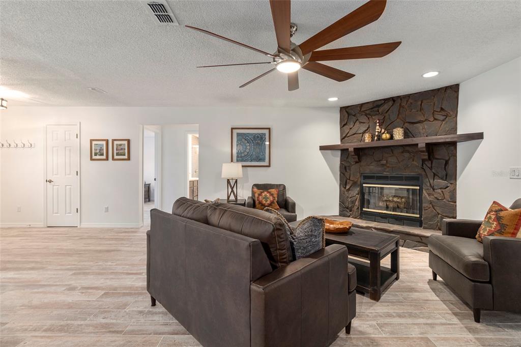 A living room features a stone fireplace, dark leather furniture, and a ceiling fan — 1900 NW 73RD TERRACE, OCALA, FL