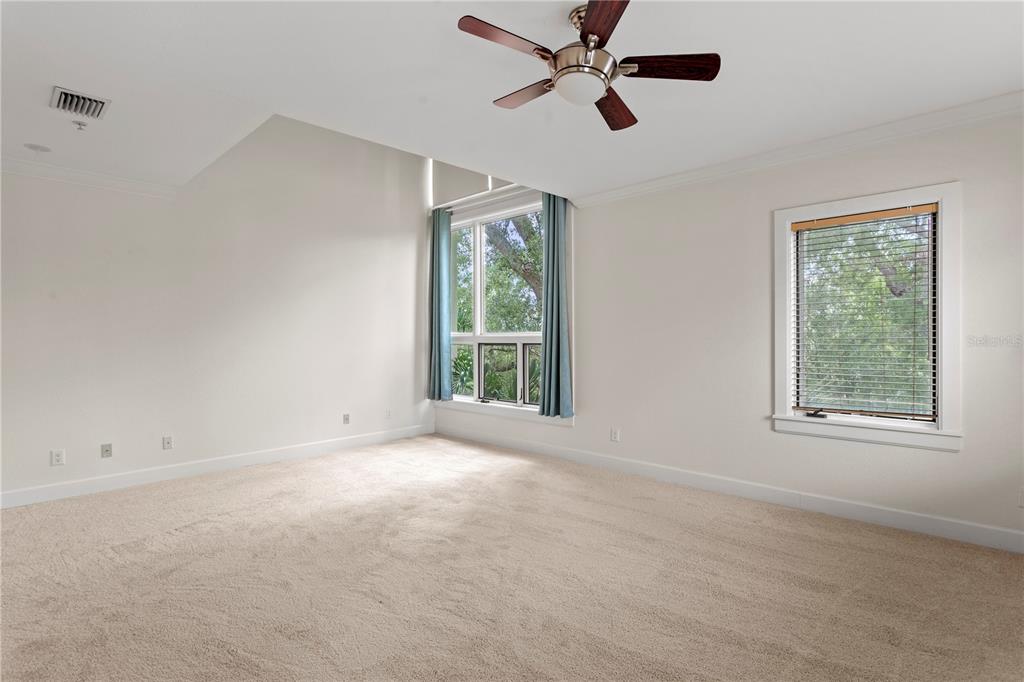 An empty bedroom features beige carpeting, a ceiling fan, and large windows with blue curtains — 512 S GLEN AVENUE, TAMPA, FL