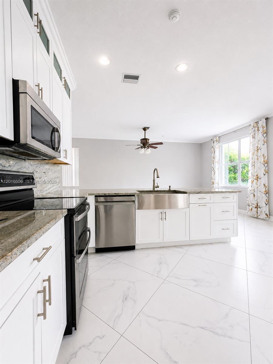 A modern kitchen features white cabinets, stainless steel appliances, a farmhouse sink, and marble flooring — 963 Falling Water Rd, Weston FL 33326, WESTON, FL