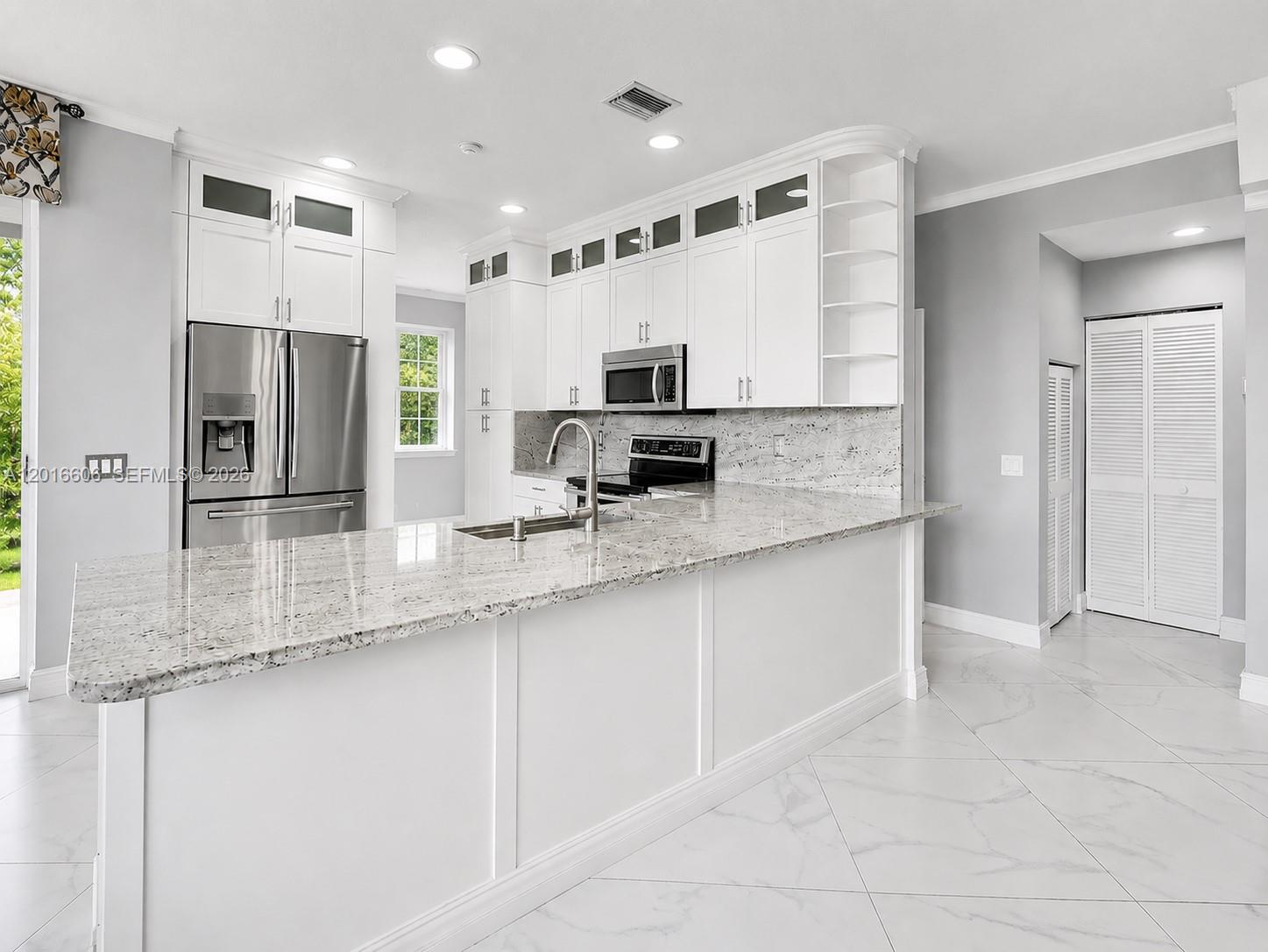 A modern kitchen features white cabinetry, granite countertops, and light-colored tile flooring — 963 Falling Water Rd, Weston FL 33326, WESTON, FL