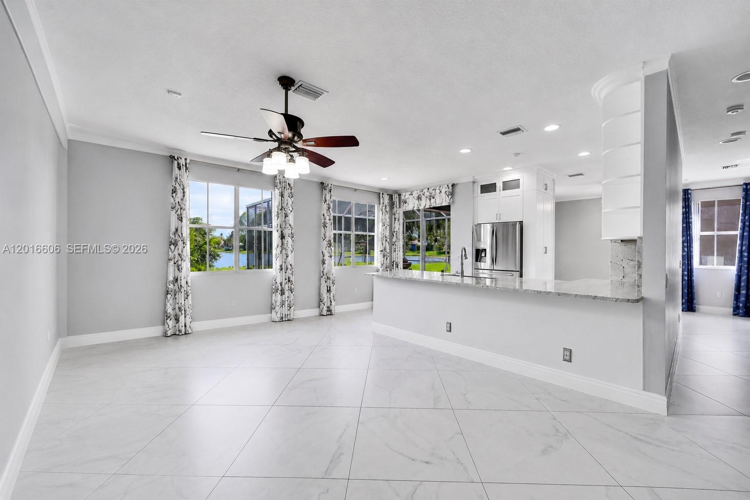 An open-concept kitchen and living area features white cabinetry, marble-look tile flooring, and lake views — 963 Falling Water Rd, Weston FL 33326, WESTON, FL