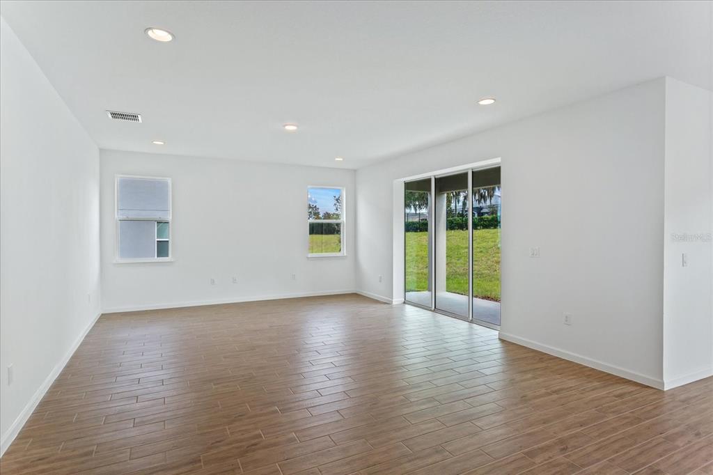 An empty room features white walls, recessed lighting, wood-look tile flooring, and sliding glass doors — 5415 NICKERBEAN STREET, APOPKA, FL