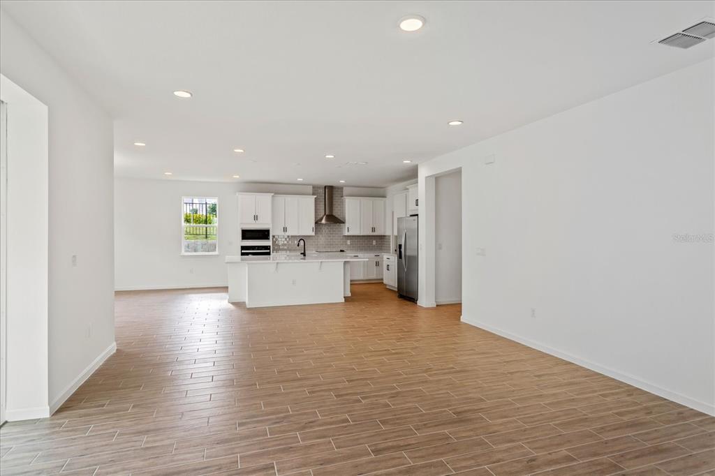 A bright, open-concept kitchen features white cabinetry, a center island, and wood-look tile flooring — 5415 NICKERBEAN STREET, APOPKA, FL