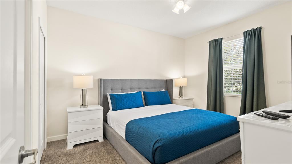 A bedroom features a gray upholstered bed, blue bedding, white nightstands, and dark green curtains — 9098 HAZARD STREET, DAVENPORT, FL