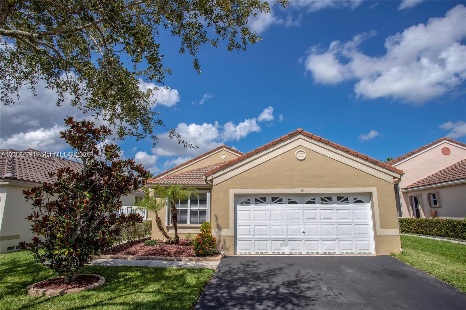 A tan single-story house features a white garage door, a tiled roof, and a front lawn — 614 Stanton Ln, Weston FL 33326, WESTON, FL