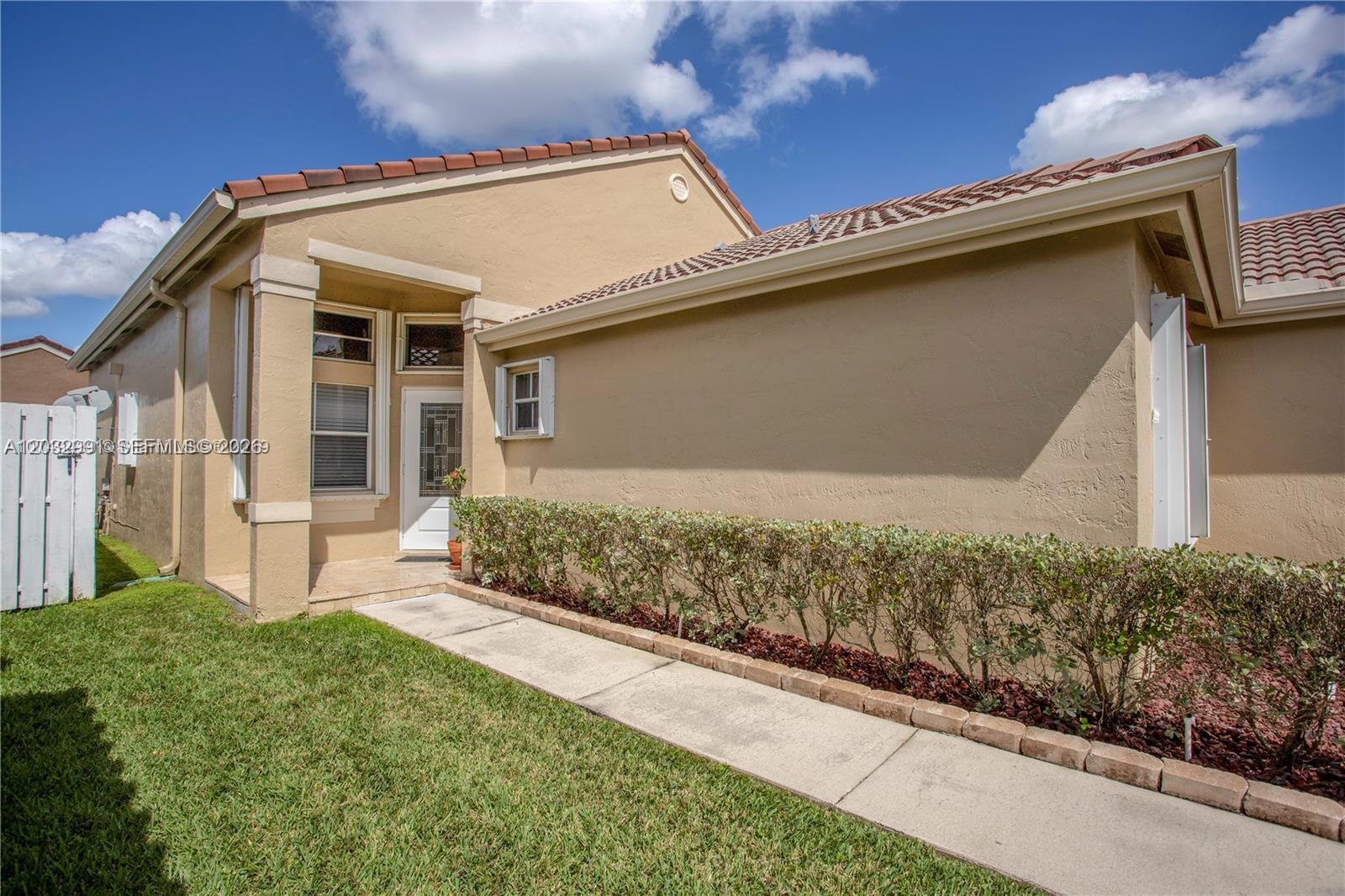 A tan stucco house exterior features a tiled roof, a walkway, and a small hedge — 614 Stanton Ln, Weston FL 33326, WESTON, FL