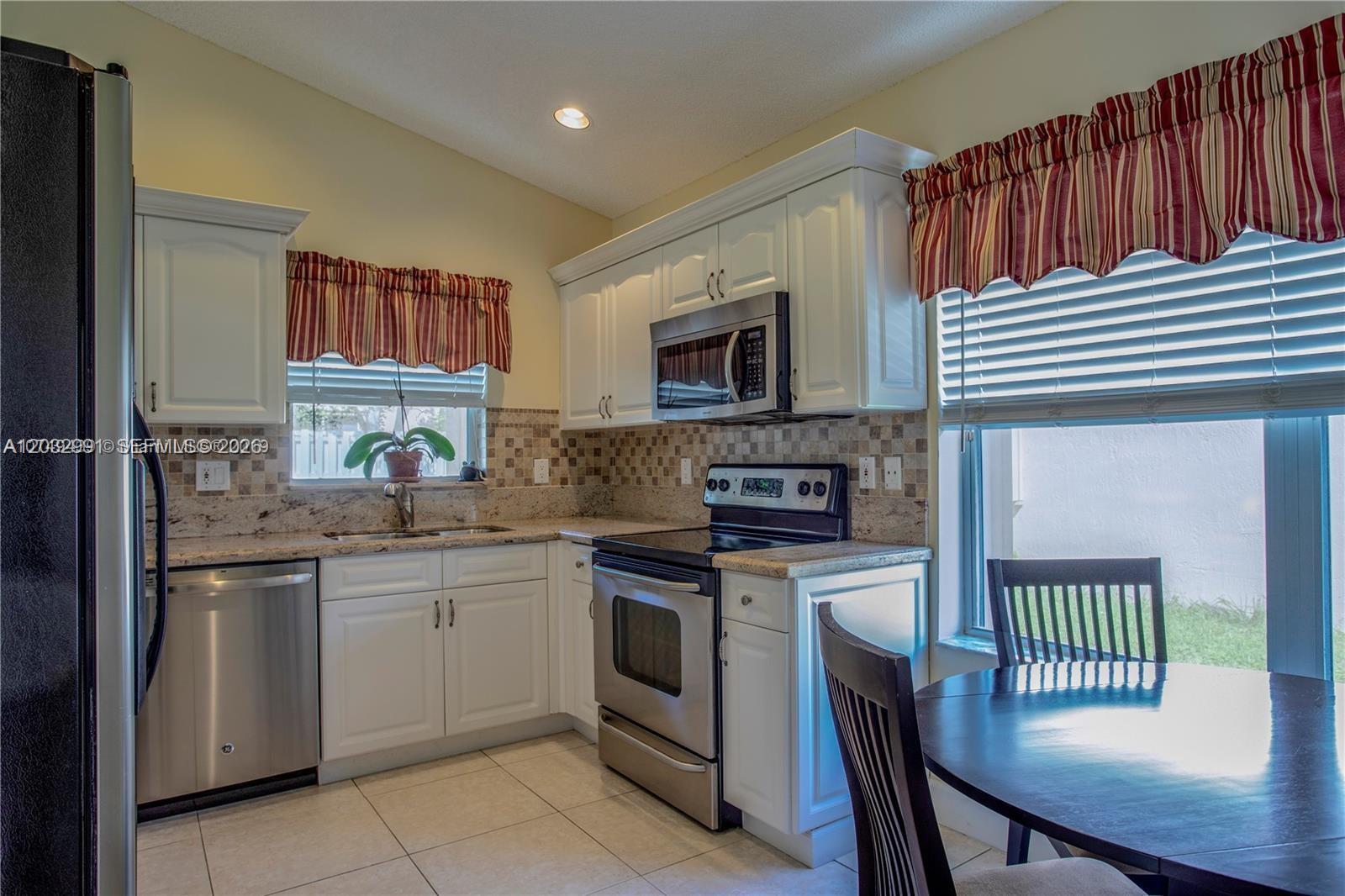 A kitchen features white cabinets, stainless steel appliances, granite countertops, and a small dining area — 614 Stanton Ln, Weston FL 33326, WESTON, FL