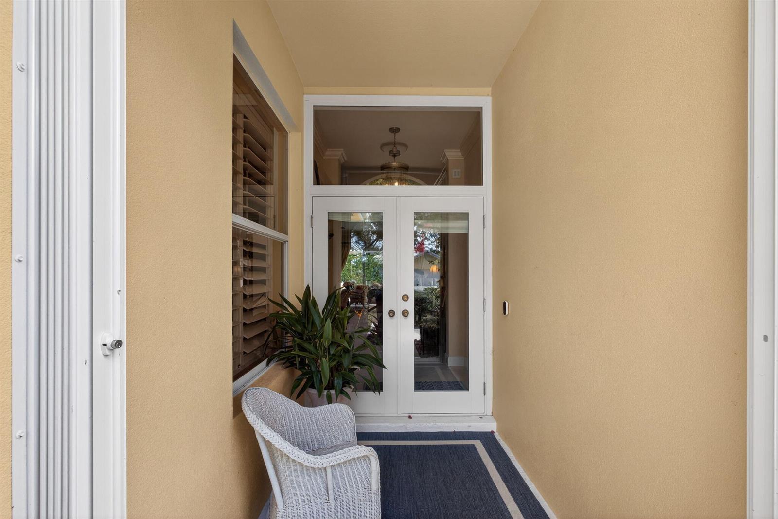 A covered entryway features a white double door, a wicker chair, and a potted plant — 1180 Gator Trail, West Palm Beach FL 33409, WEST PALM BEACH, FL
