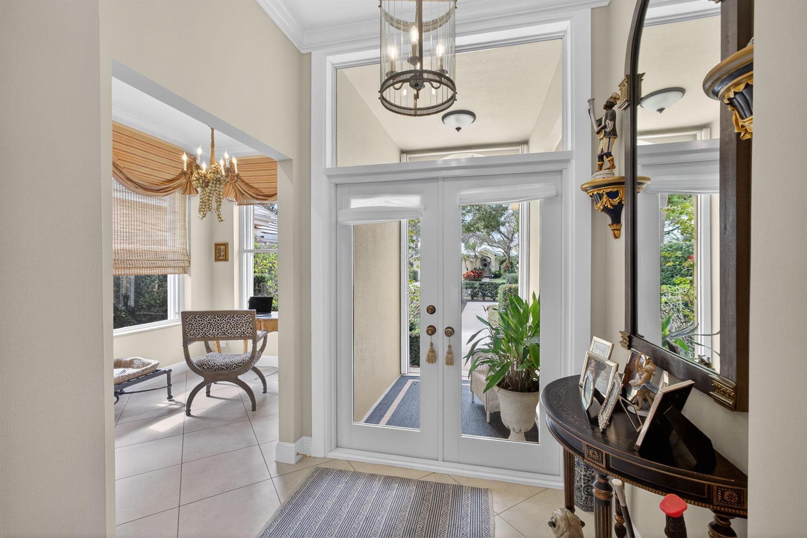 An entryway features a double glass door, a chandelier, and a view into a room — 1180 Gator Trail, West Palm Beach FL 33409, WEST PALM BEACH, FL