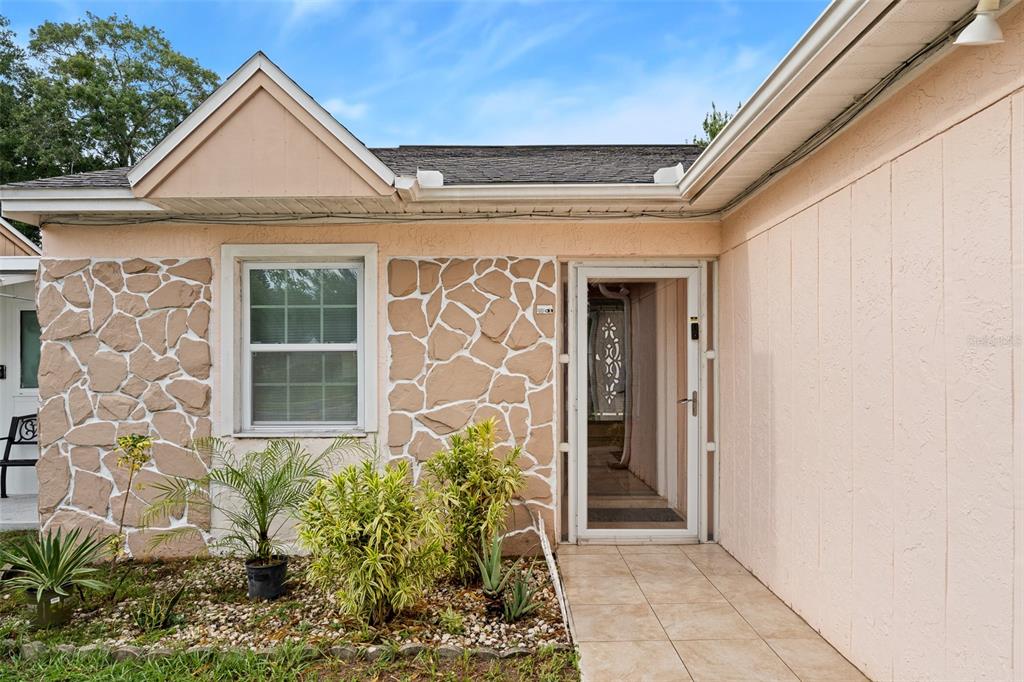 The exterior of a house features peach-colored walls, stone accents, a tiled walkway, and landscaping — 8903 CAMINO VILLA, TAMPA, FL