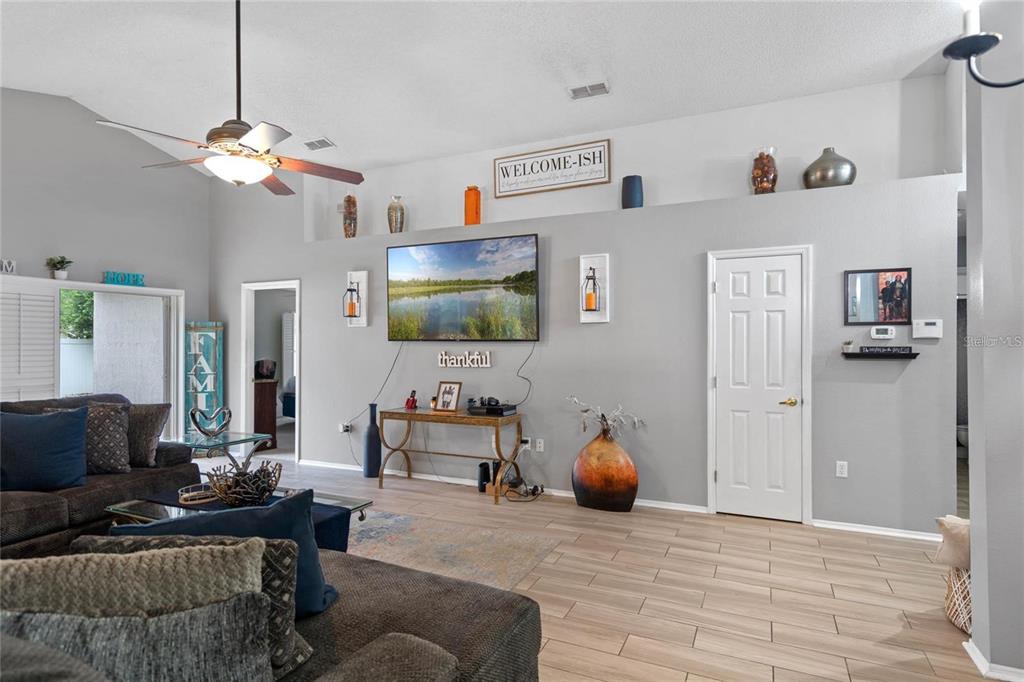 A living room features a vaulted ceiling, light wood-look tile flooring, and a wall-mounted television — 541 HEATHER GLEN DR, WINTER HAVEN, FL