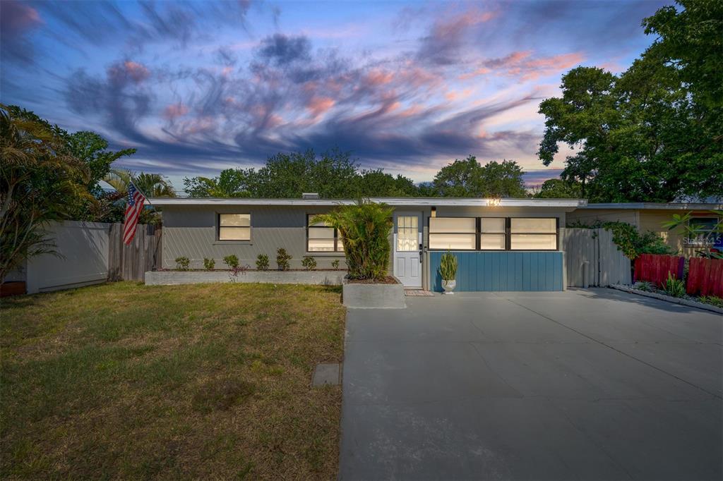 A single-story house with a gray exterior, blue accents, and a concrete driveway at dusk — 11919 102ND STREET, LARGO, FL