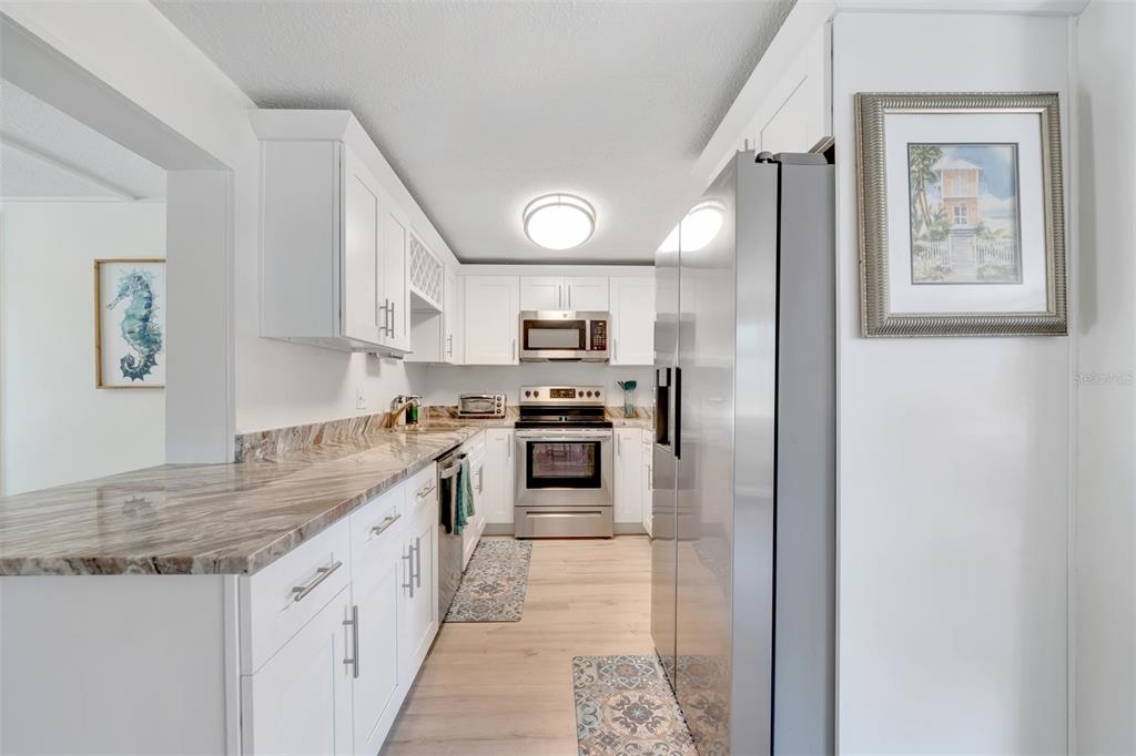 A galley-style kitchen features white cabinets, stainless steel appliances, and a marble-patterned countertop — 11919 102ND STREET, LARGO, FL