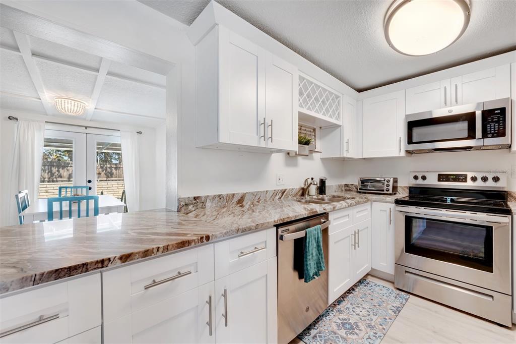 A kitchen features white cabinets, granite countertops, stainless steel appliances, and a view into a dining area — 11919 102ND STREET, LARGO, FL