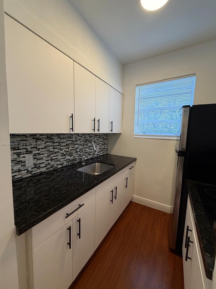 A kitchen features white cabinets, black granite countertops, a mosaic tile backsplash, and wood flooring — 1525 Meridian Ave # 108, Miami Beach FL 33139, MIAMI BEACH, FL