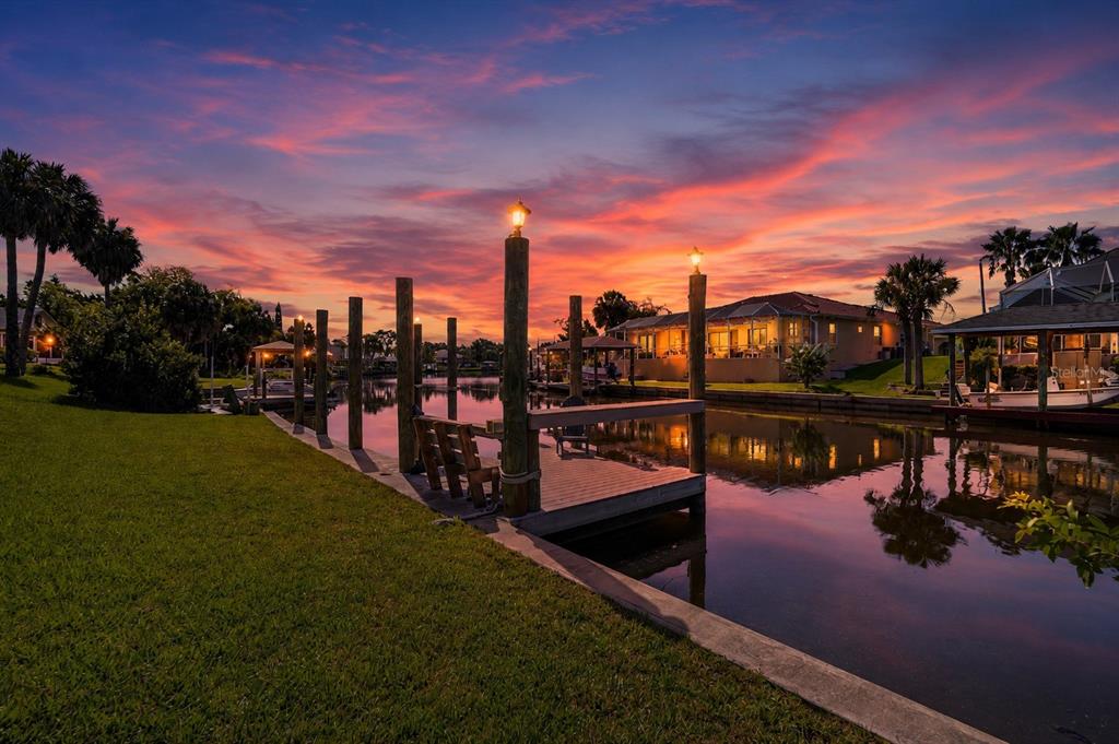 A wooden dock extends into a canal at sunset with palm trees and houses nearby — 109 CORAL REEF COURT N, PALM COAST, FL