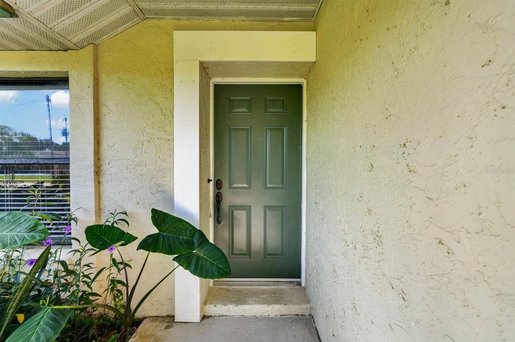 A green front door is set into a beige stucco wall beside a window — 109 CORAL REEF COURT N, PALM COAST, FL