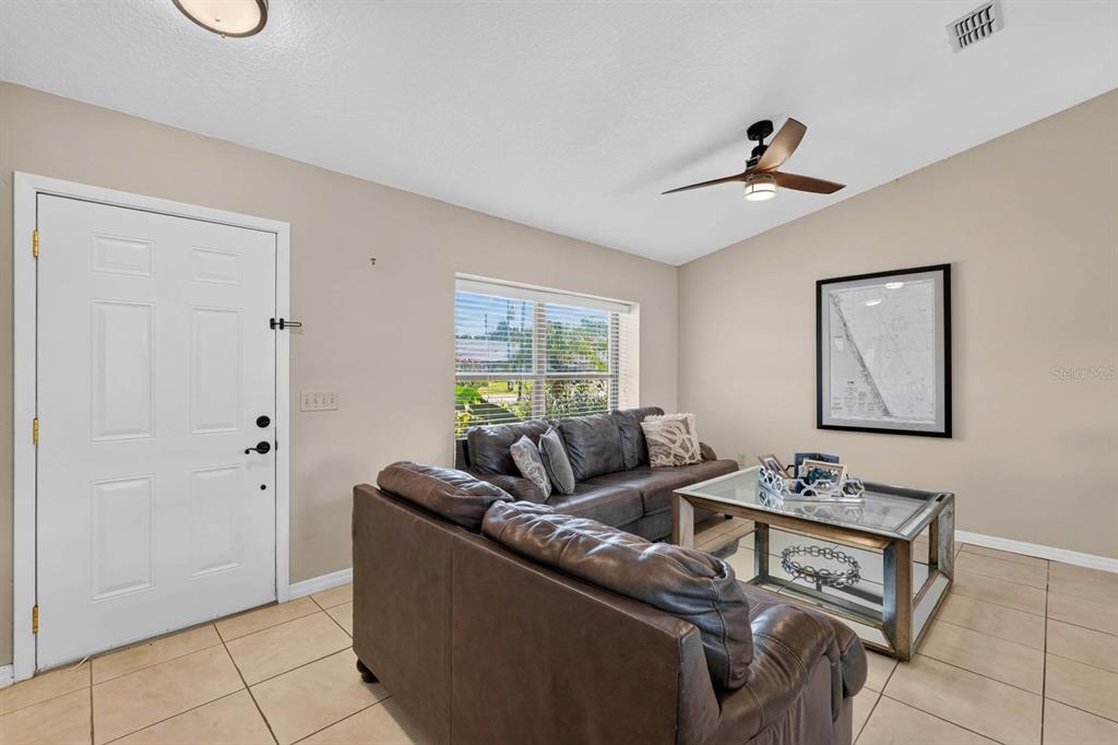 A living room features a brown leather sectional sofa, a glass coffee table, and tile flooring — 109 CORAL REEF COURT N, PALM COAST, FL