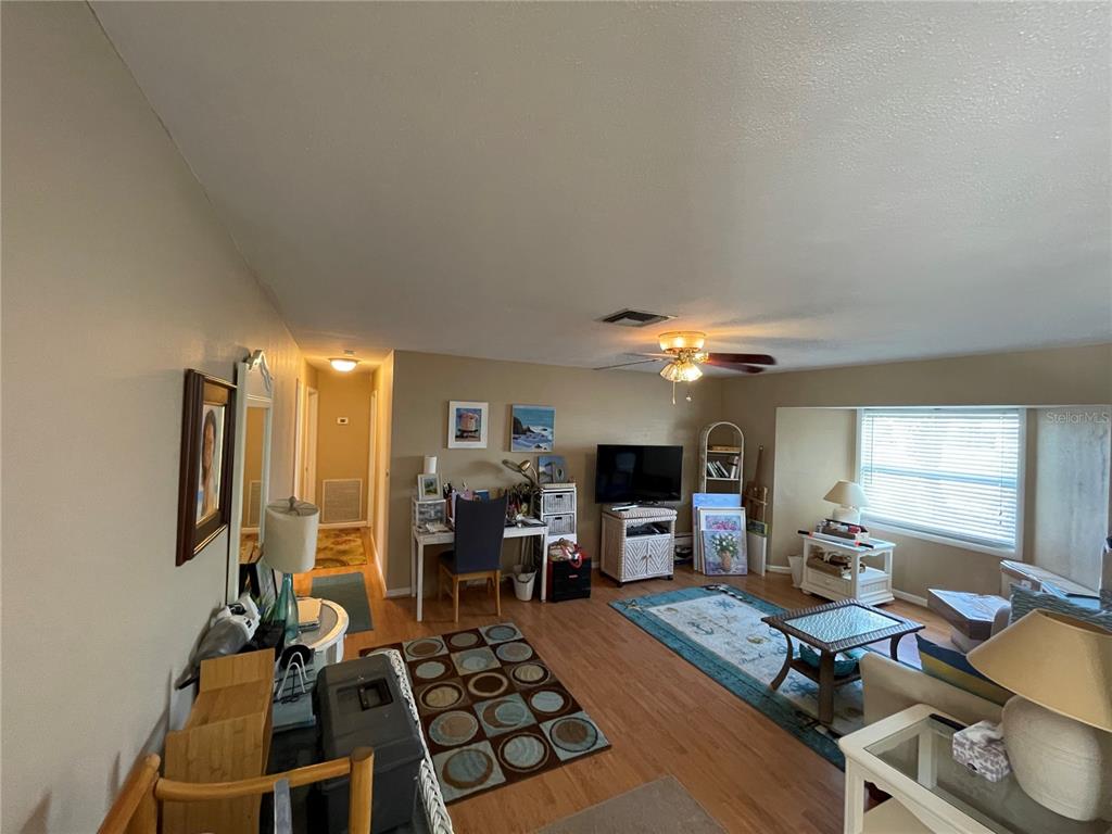 A living room with wood flooring, a desk area, a television, and a large window — 9 ANNAPOLIS LANE, ROTONDA WEST, FL