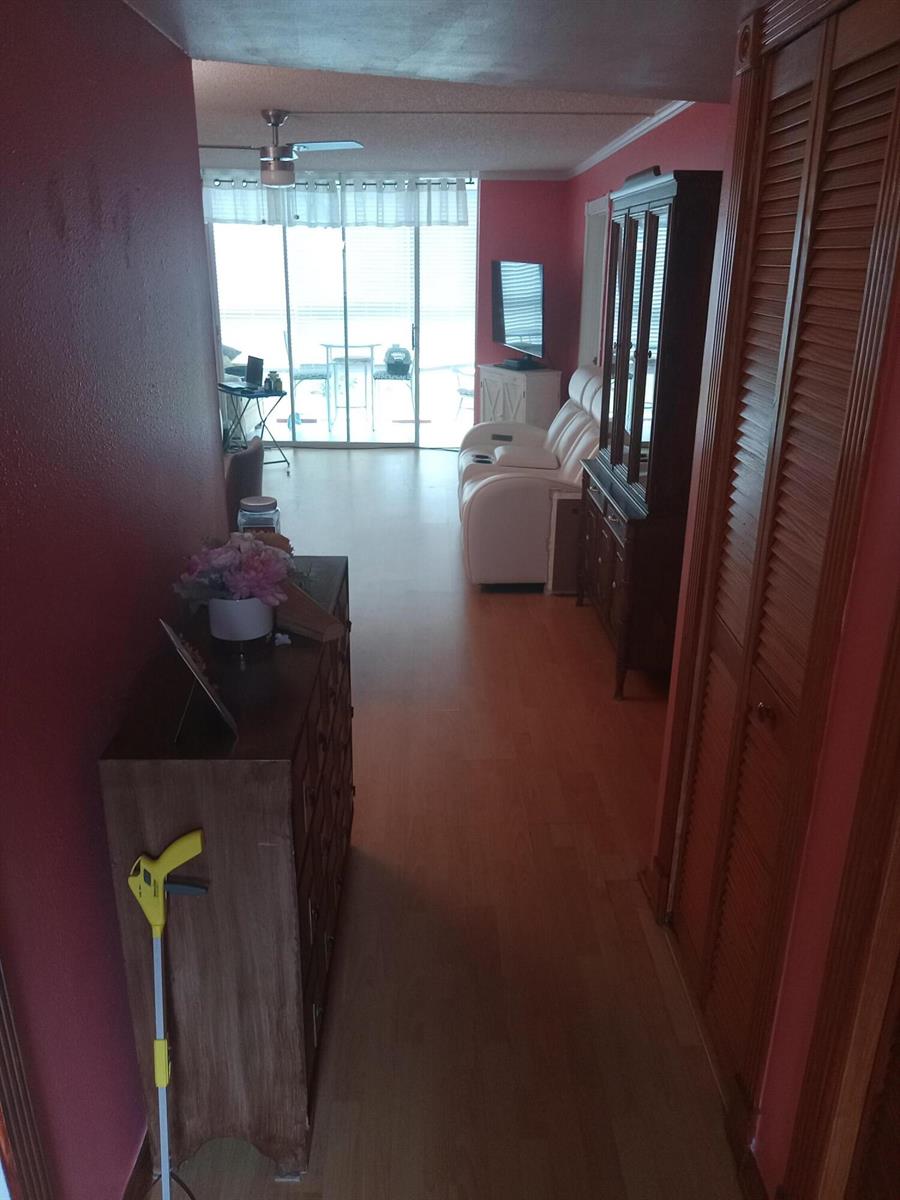 A hallway with wood flooring leads to a living area with a sliding glass door — 2901 E Sunrise Lakes Drive E # 202, Sunrise FL 33322, SUNRISE, FL