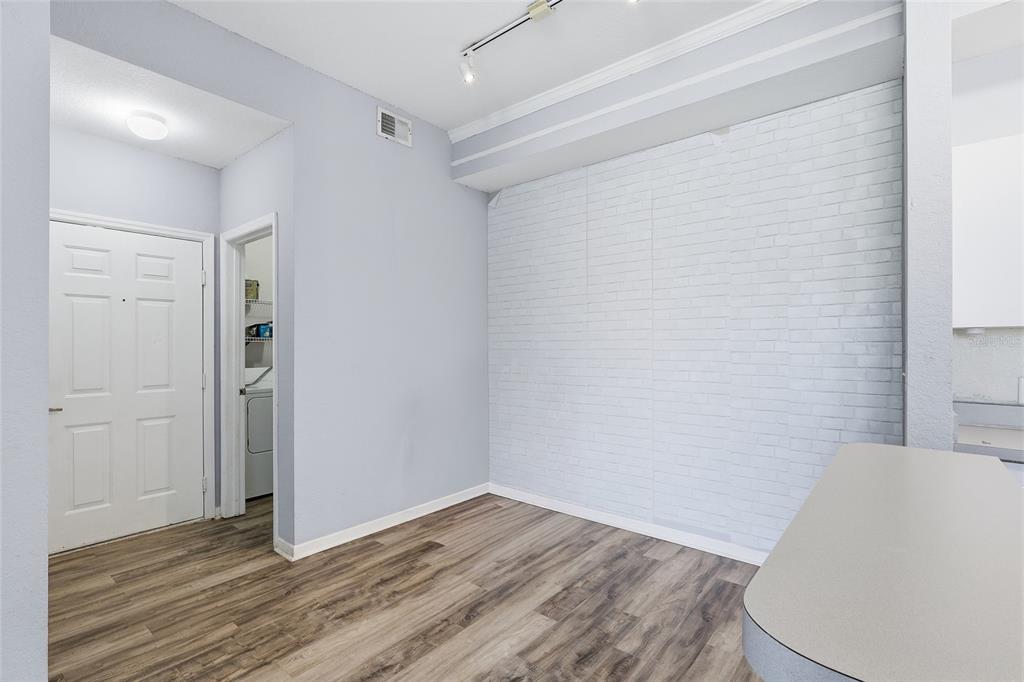 An interior view of a room featuring light blue walls, wood-look flooring, and a brick-patterned wall — 17106 CARRINGTON PARK DRIVE UNIT 623, TAMPA, FL