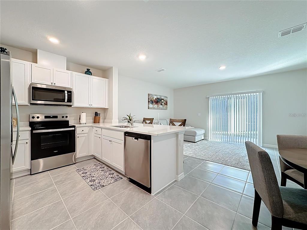 A kitchen with white cabinets, stainless steel appliances, and an island opens to a living area — 3140 GOOSE ROAD, DAVENPORT, FL