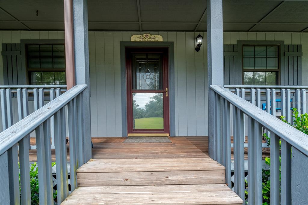 A wooden staircase leads to a covered front porch with a red door and railings — 5127 SW COUNTY ROAD 18A, LAKE BUTLER, FL