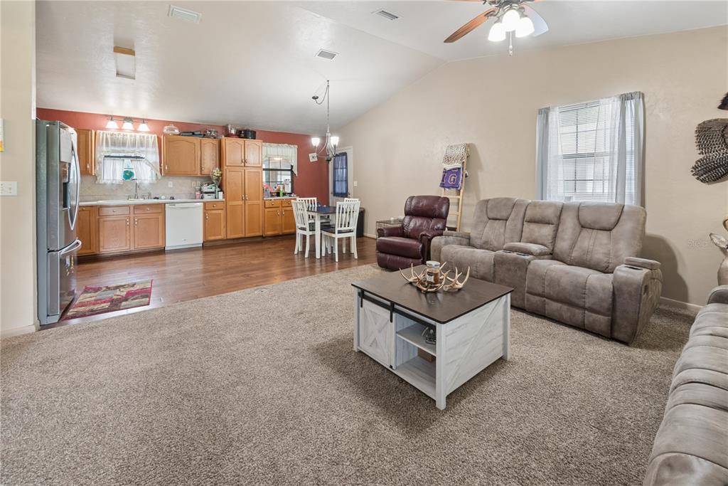 An open-concept living room and kitchen area with carpeted floors, wood cabinets, and neutral walls — 5127 SW COUNTY ROAD 18A, LAKE BUTLER, FL
