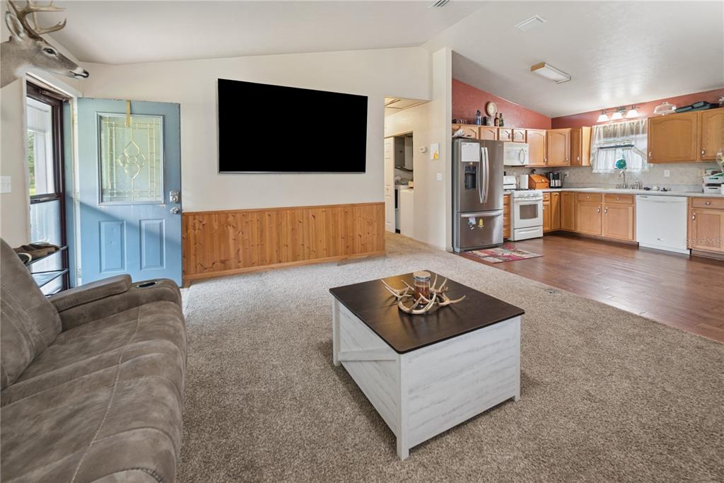 A living room with carpeted floors and wood wainscoting opens into a kitchen with wood cabinets — 5127 SW COUNTY ROAD 18A, LAKE BUTLER, FL