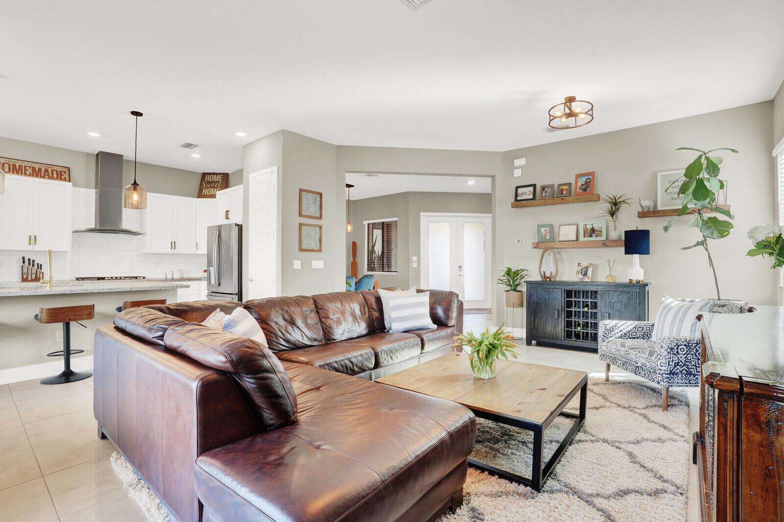A living room with a brown leather sectional, wooden coffee table, and an open kitchen — 10767 Pacifica Way, Parkland FL 33076, PARKLAND, FL