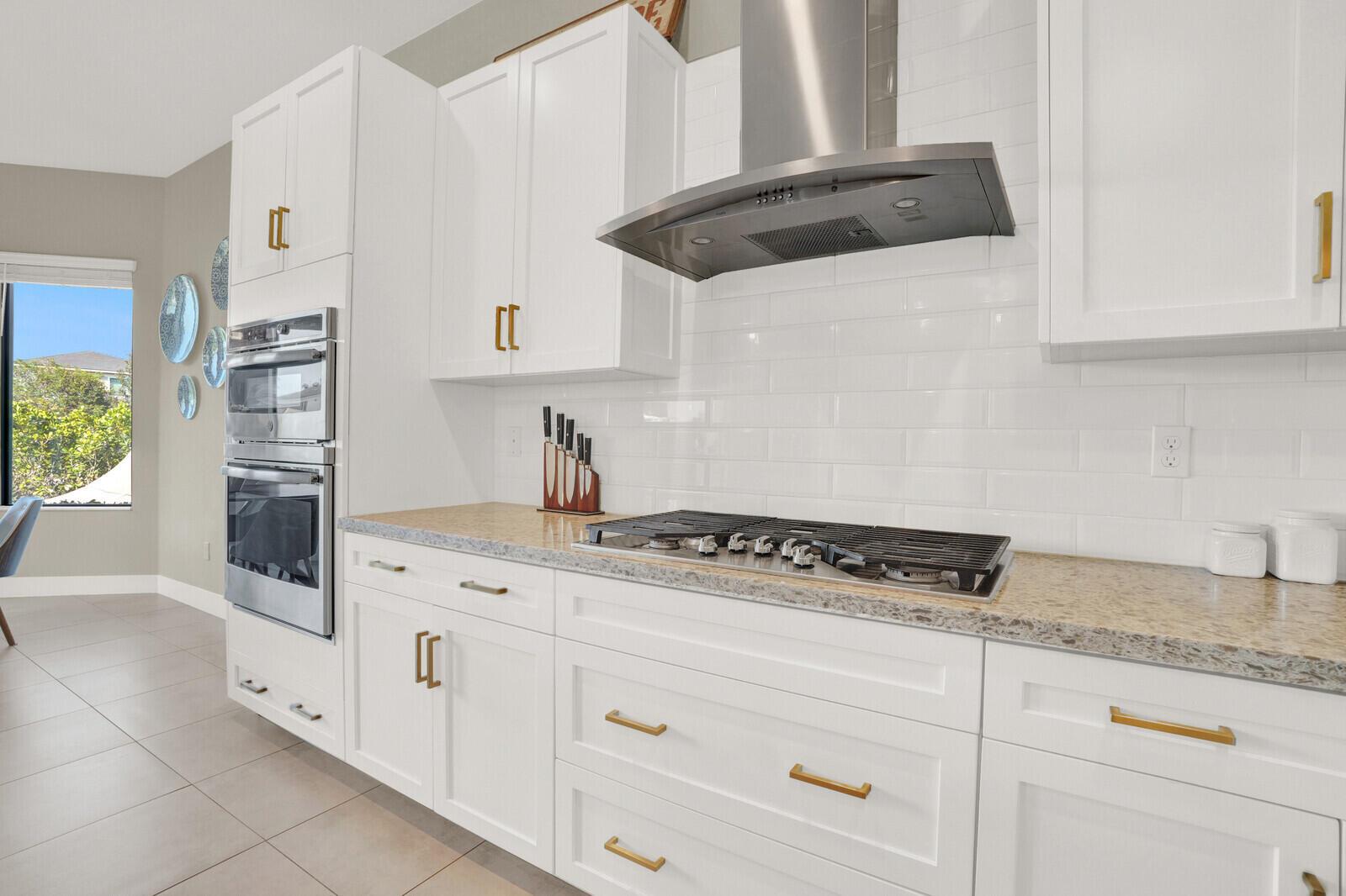 A kitchen features white cabinets, gold hardware, a gas cooktop, and a stainless steel oven — 10767 Pacifica Way, Parkland FL 33076, PARKLAND, FL