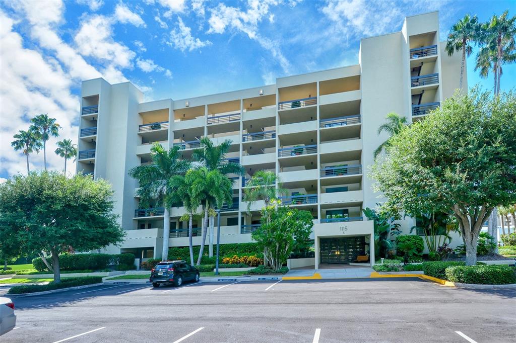 A multi-story residential building with balconies and palm trees stands above a paved parking lot — 1115 GULF OF MEXICO DRIVE UNIT 401, LONGBOAT KEY, FL