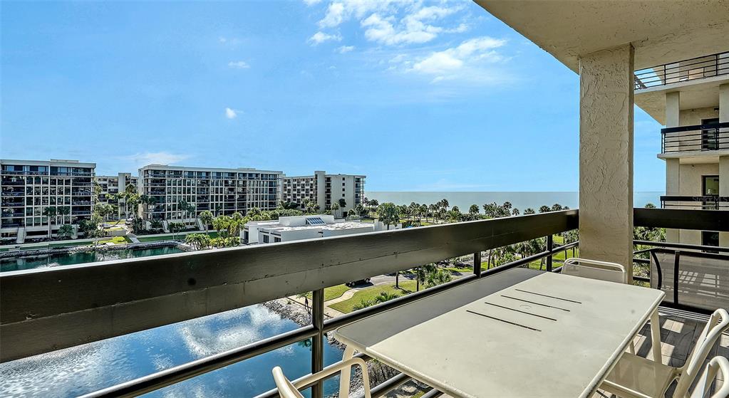 A balcony with a table and chairs overlooks a water feature and the distant ocean — 1115 GULF OF MEXICO DRIVE UNIT 401, LONGBOAT KEY, FL
