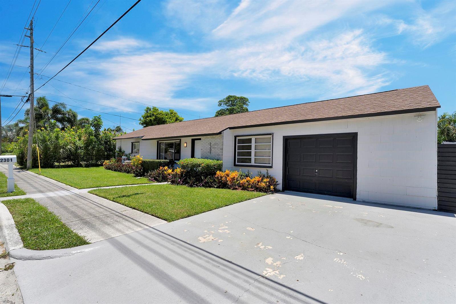 A single-story house with a white exterior, dark garage door, and a landscaped front yard — 2301 Ridgeway Avenue, West Palm Beach FL 33401, WEST PALM BEACH, FL
