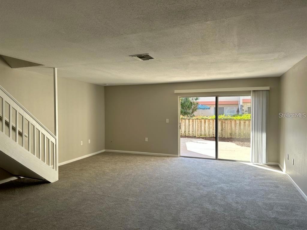 An empty living room features gray carpeting, neutral walls, a staircase, and a sliding glass door — 5855 16TH STREET S UNIT 6, ST PETERSBURG, FL